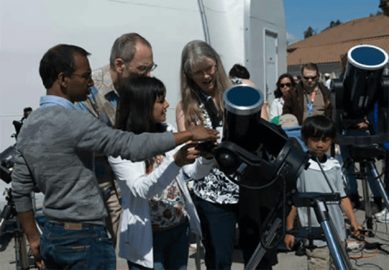 Sun watchers gather around telescopes fitted with white light solar filters.
